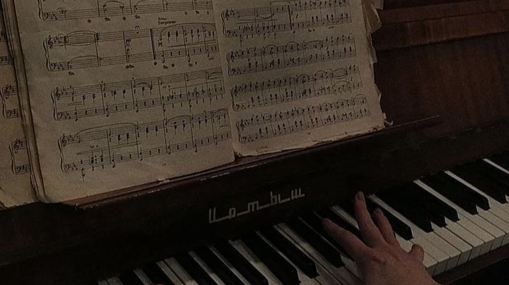 hand playing a piano with vintage sheet music on the stand