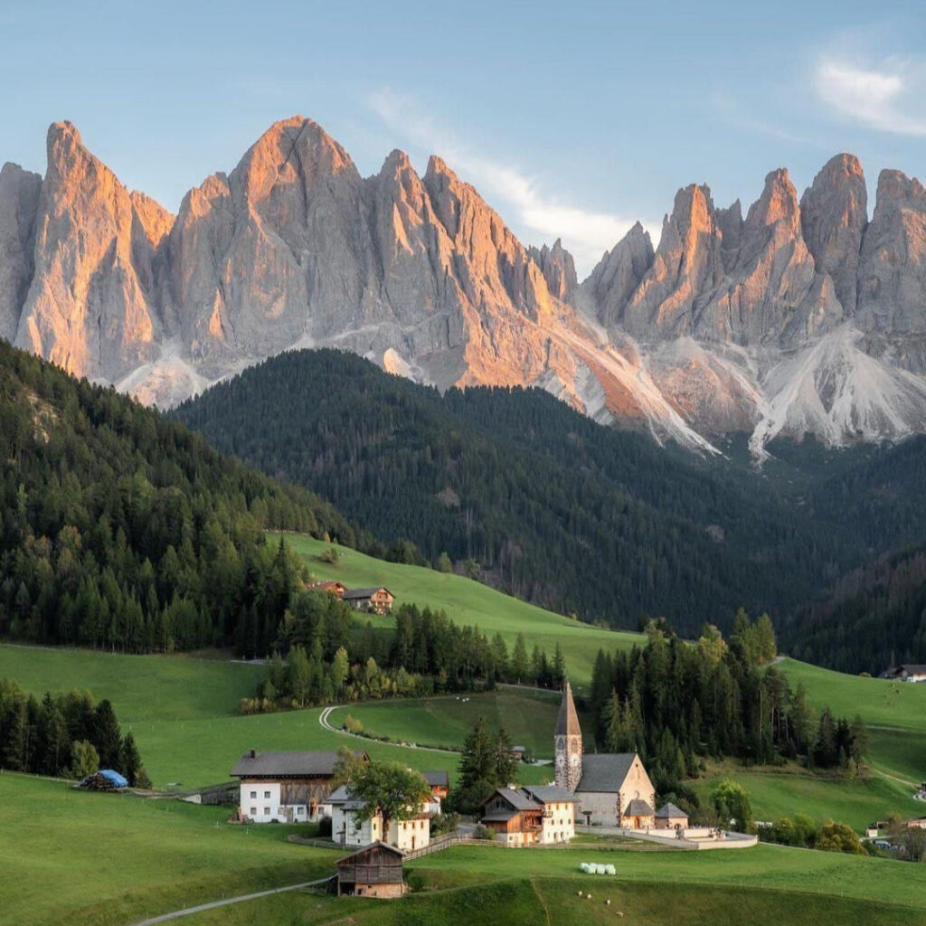 Scenic mountain village in the Dolomites of northern Italy at sunrise with alpine peaks and green valleys.